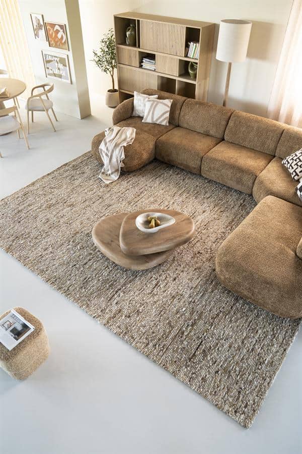 Knusse hoekbank in warm beige stoffen bekleding met bijpassende sierkussens, houten salontafel en moderne interieurdecoratie, perfect voor een stijlvolle woonkamer.