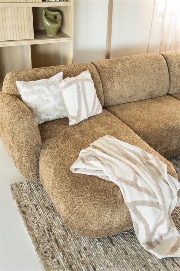 Moderne lichtbruine stoffen hoekbank met witte decoratieve kussens en een plaid, passend in een eigentijdse woonkamer met houten meubels en een zachte sfeer.