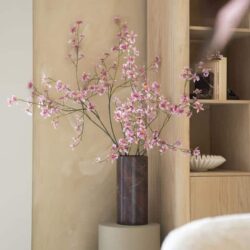 Elegant bloemenvaas met roze bloesems op een houten meubel bij Mokana Meubelen.