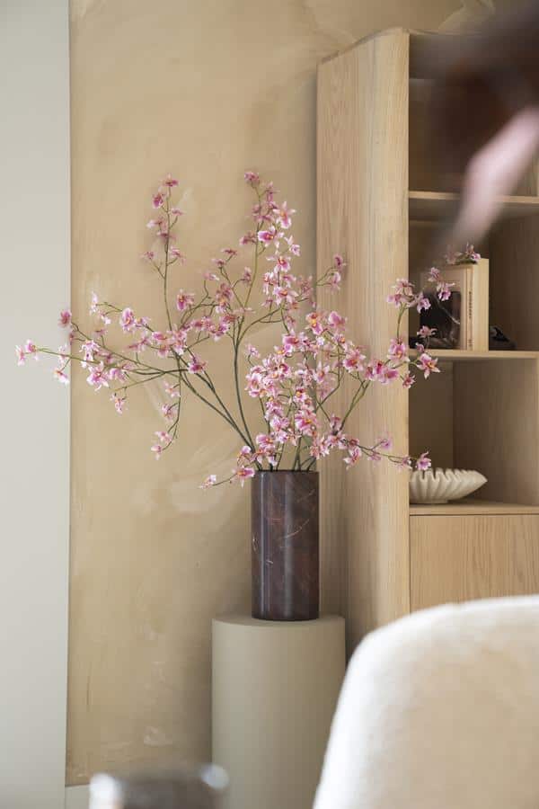 Elegant bloemenvaas met roze bloesems op een houten meubel bij Mokana Meubelen.