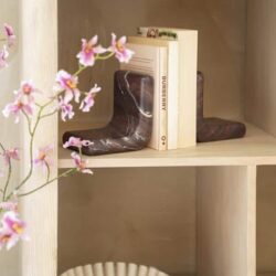 Marmeren schoenenbeeldjes op houten boekenkast gecombineerd met boeken en witte vaas, elegante decoratie voor interieur, stijlvolle meubelaccessoires.