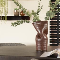 Unieke siervaas met eucalyptus takken op houten eettafel, modern interieur met wandplanken en decoratieve potten, stijlvol en natuurlijk sfeer in huis.