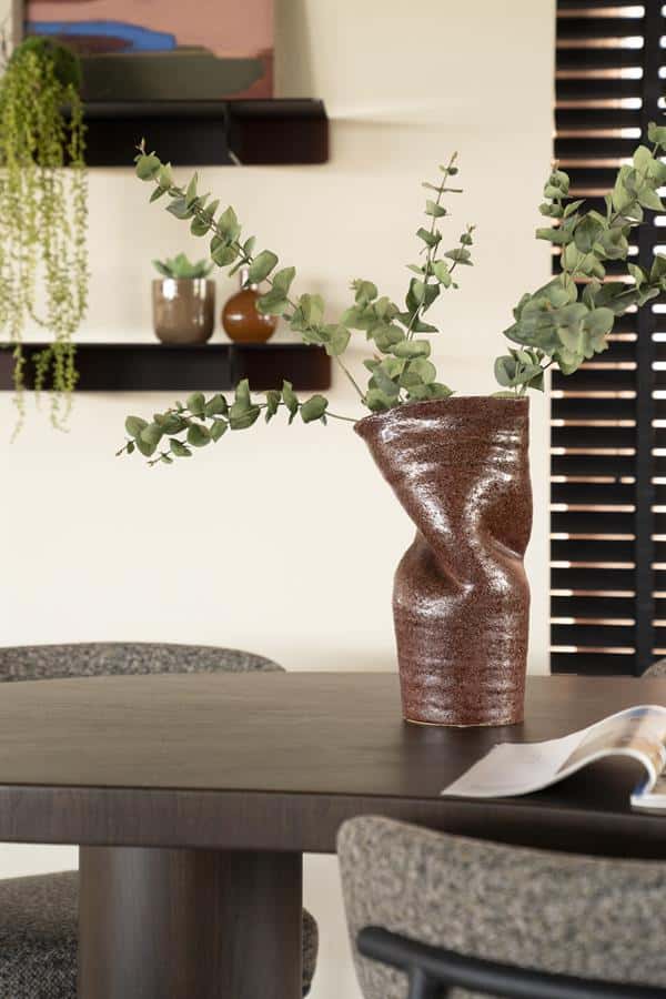 Unieke siervaas met eucalyptus takken op houten eettafel, modern interieur met wandplanken en decoratieve potten, stijlvol en natuurlijk sfeer in huis.