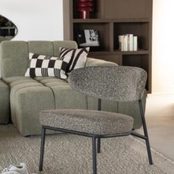 Moderne fauteuil met metalen frame en stoffen bekleding in een stijlvolle woonkamer, naast een lichtgroon bank en een houten boekenkast, perfect voor modern interieur design.