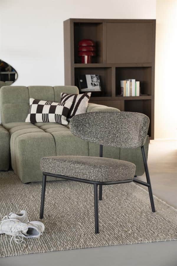 Moderne fauteuil met metalen frame en stoffen bekleding in een stijlvolle woonkamer, naast een lichtgroon bank en een houten boekenkast, perfect voor modern interieur design.