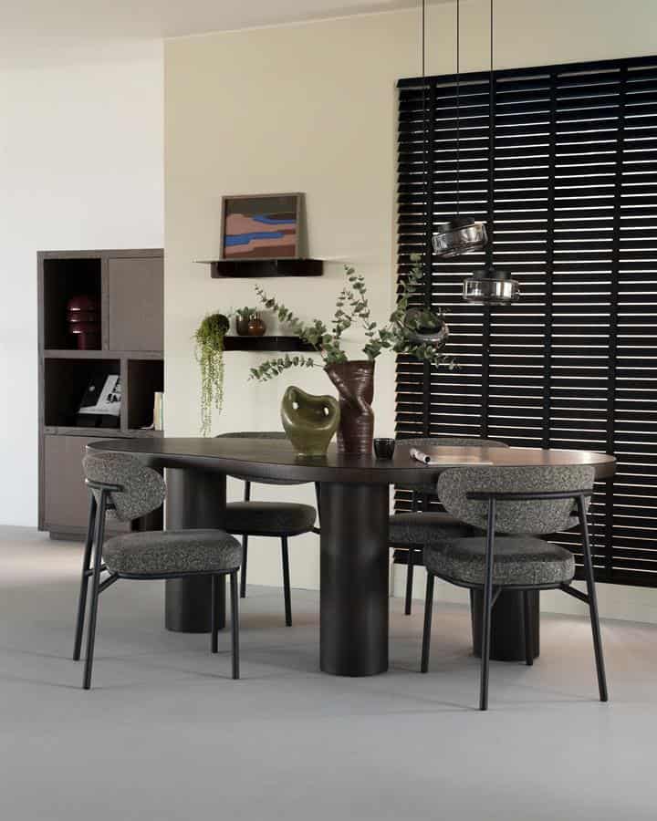 Elegante zwarte eettafel met drie bijpassende fauteuils en decoratieve vazen en bladeren, perfect voor een moderne en stijlvolle eetkamer.