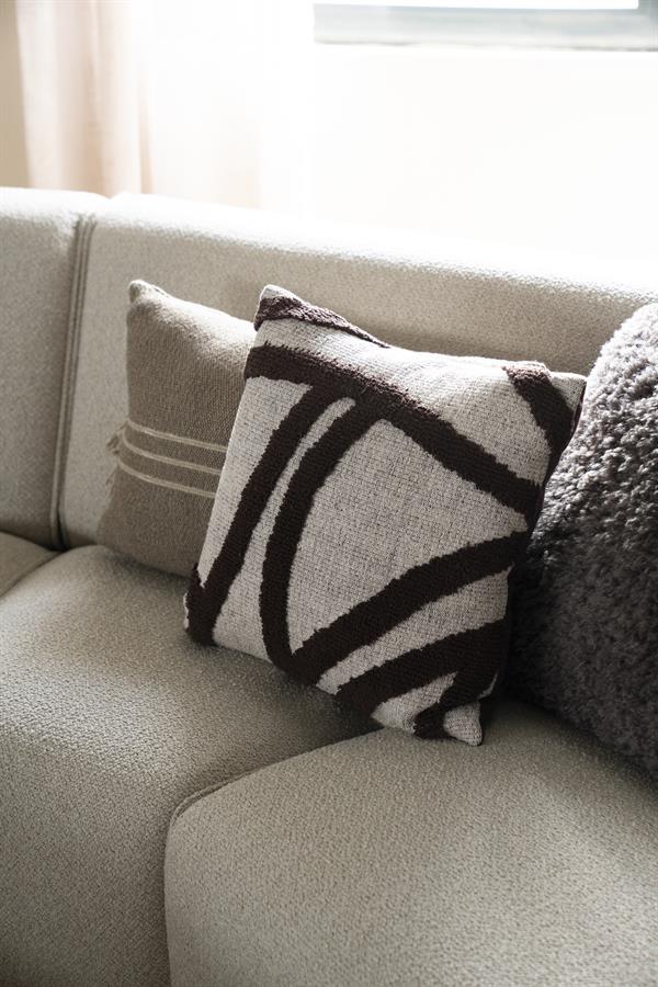 Zwarte en witte design patterned kussen op een beige bank, modern en stijlvol woontextiel.