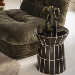 Elegante zwarte bijzettafel met witte lijnen, naast een gezellige velvet bank, decoratief servies en karaf voor een stijlvolle woonkamer uitstraling.