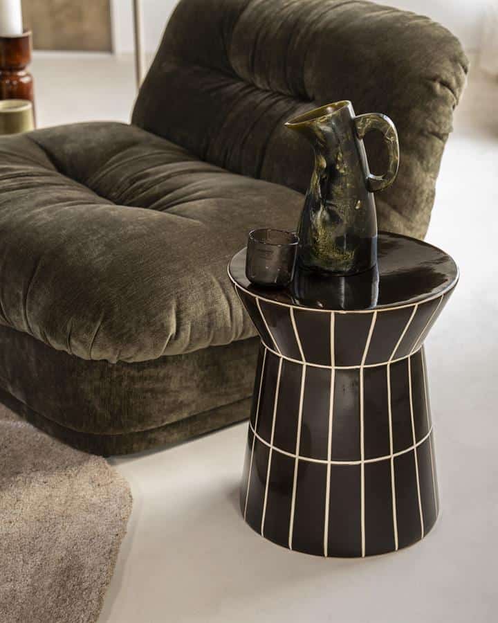 Elegante zwarte bijzettafel met witte lijnen, naast een gezellige velvet bank, decoratief servies en karaf voor een stijlvolle woonkamer uitstraling.