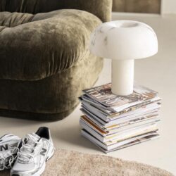Moderne witte marmeren tafellamp op stapel tijdschriften naast bank in woonkamer.