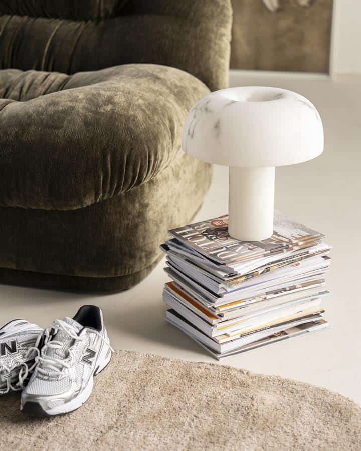 Moderne witte marmeren tafellamp op stapel tijdschriften naast bank in woonkamer.