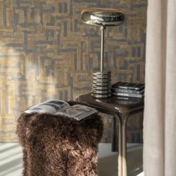 Chique bureaulamp en accessoires op een zwart bijzettafeltje met boeken en een zachte, donzige poef in een modern interieur.