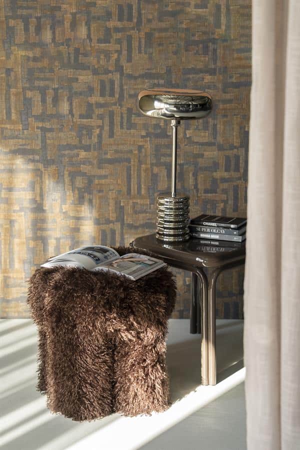 Chique bureaulamp en accessoires op een zwart bijzettafeltje met boeken en een zachte, donzige poef in een modern interieur.