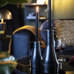 Zilveren kandelaars met brandende kaarsen op een zwart tafelblad in een sfeervolle woonkamer setting.