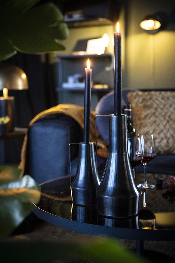 Zilveren kandelaars met brandende kaarsen op een zwart tafelblad in een sfeervolle woonkamer setting.