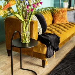 Ramenfoto van een stijlvolle woonkamer met een vintage gele velvet bank, kleurrijke bloemen in een glazen vaas en moderne meubels, perfect voor een warm en trendy interieur.