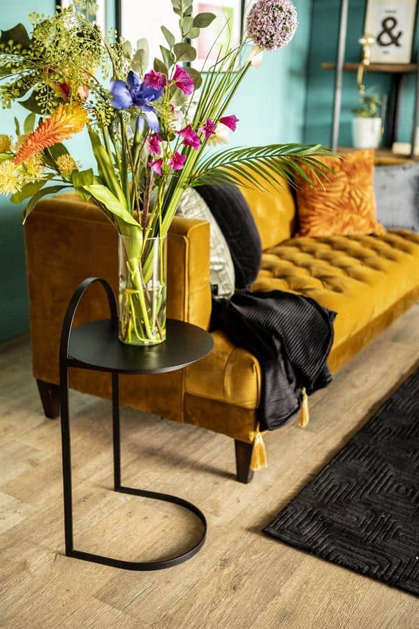 Ramenfoto van een stijlvolle woonkamer met een vintage gele velvet bank, kleurrijke bloemen in een glazen vaas en moderne meubels, perfect voor een warm en trendy interieur.