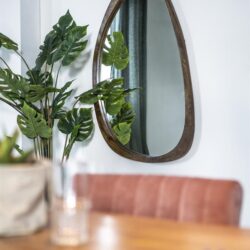 Comfortabel eettafel met ronde spiegel en groene kamerplant in modern interieur.