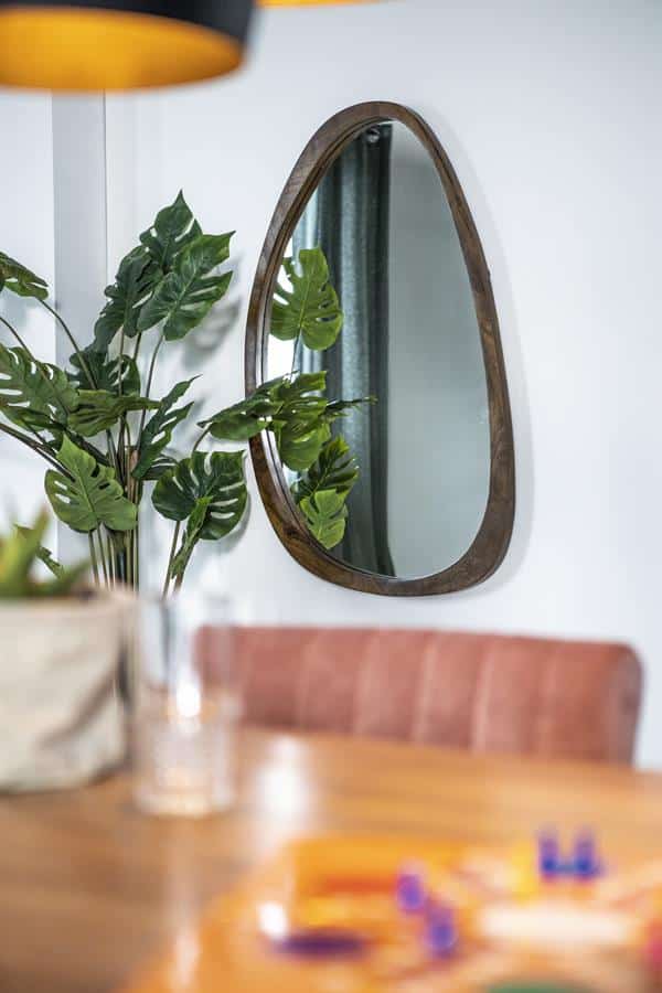 Comfortabel eettafel met ronde spiegel en groene kamerplant in modern interieur.