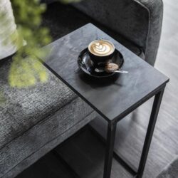 Kleine zwarte bijzettafel naast een comfortabele bank met een kopje koffie en koekje, ideaal voor moderne woonkamers en interieurs.