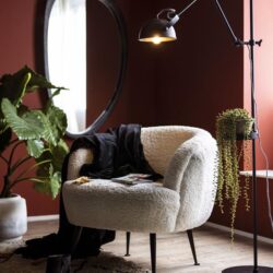 Volle, witte, zachte armstoel in modern interieur met warme wandkleur en groene planten.