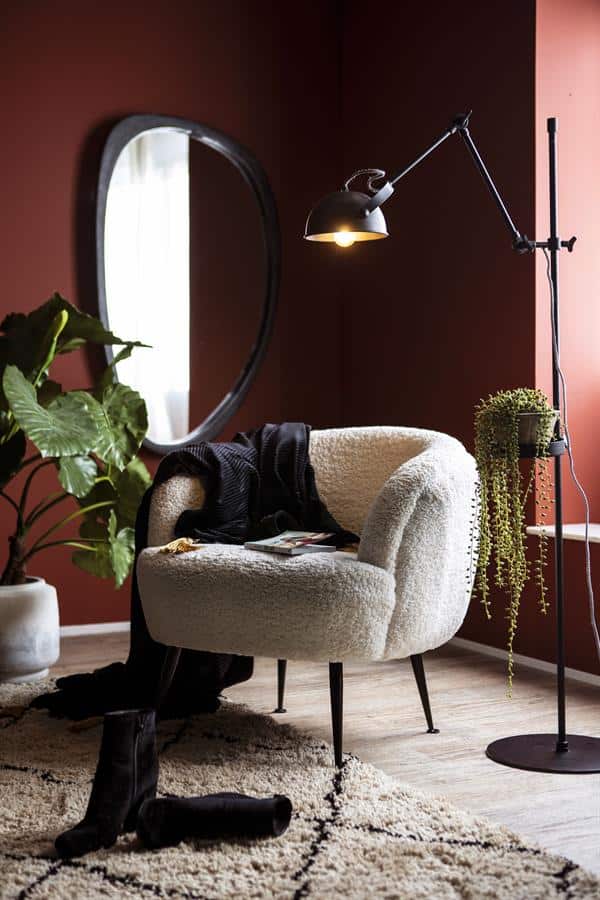 Volle, witte, zachte armstoel in modern interieur met warme wandkleur en groene planten.