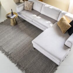 Rustieke witte bank met loungebank en sierkussens in een modern interieur, houten boekenkast, grijze zachte vloerkleed en bijzettafel, stijlvolle woonkamermeubels van Mokana Meubelen, houten decor, gezellige woonruimte.