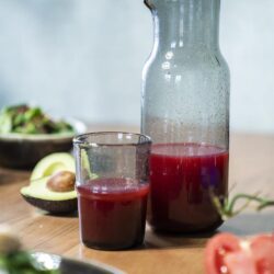 Geniet van versgeperst vruchtensap in een stijlvolle glazen karaf en glas, met verse avocado en tomaat op de houten tafel, perfect voor een gezond ontbijt of lunch.