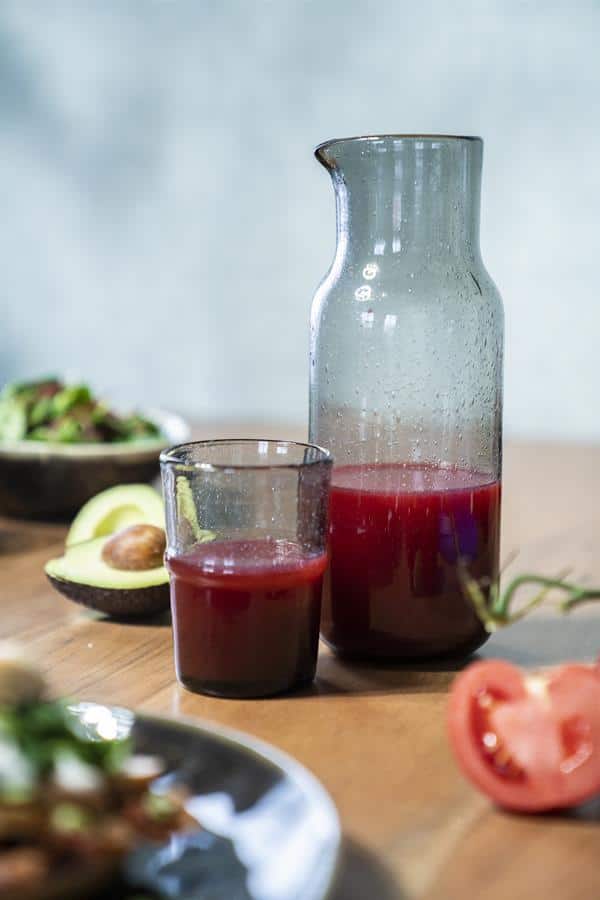 Geniet van versgeperst vruchtensap in een stijlvolle glazen karaf en glas, met verse avocado en tomaat op de houten tafel, perfect voor een gezond ontbijt of lunch.