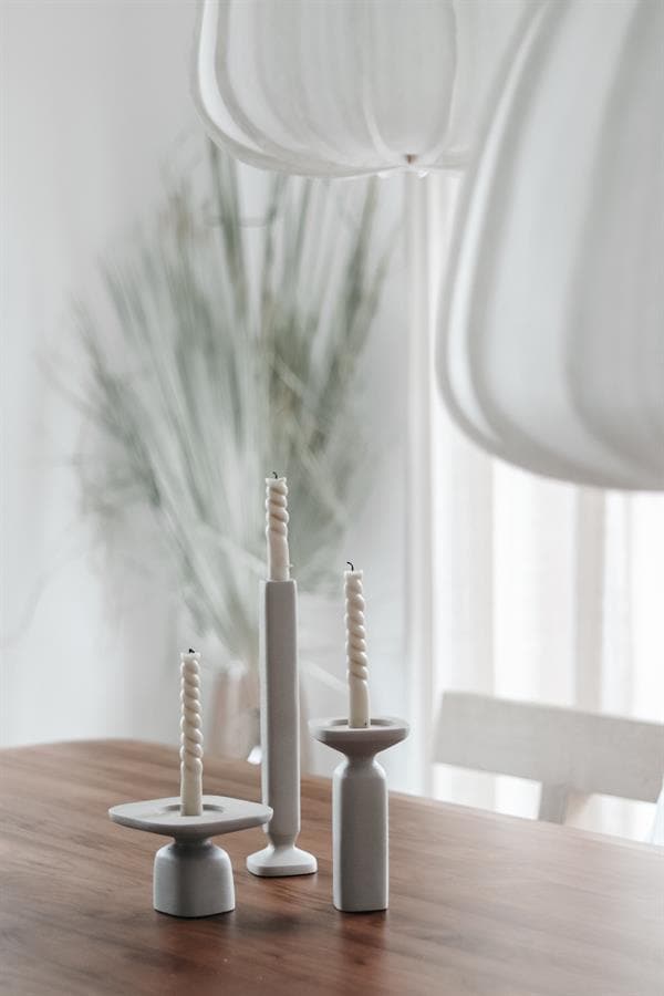 Elegante witte kaarsenhouders met gedraaide kaarsen op een houten eettafel, perfect voor een sfeervolle en moderne interieurdecoratie.