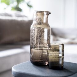 Glas en waterfles op een bijzettafel in een modern interieur, nabewerkt met natuurlijke en minimalistische stijl, perfect voor stijlvolle huishouddecoratie.