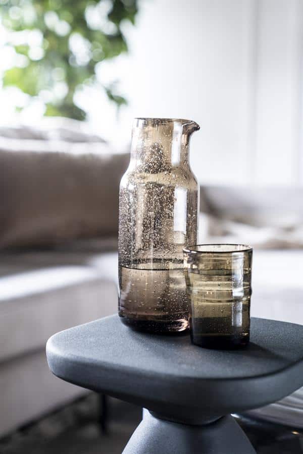 Glas en waterfles op een bijzettafel in een modern interieur, nabewerkt met natuurlijke en minimalistische stijl, perfect voor stijlvolle huishouddecoratie.