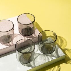Set van vier glazen op een witte dienblad met een gele achtergrond, stijlvolle en moderne uitstraling, perfect voor interieurdecoratie en servies van Mokana Meubelen.