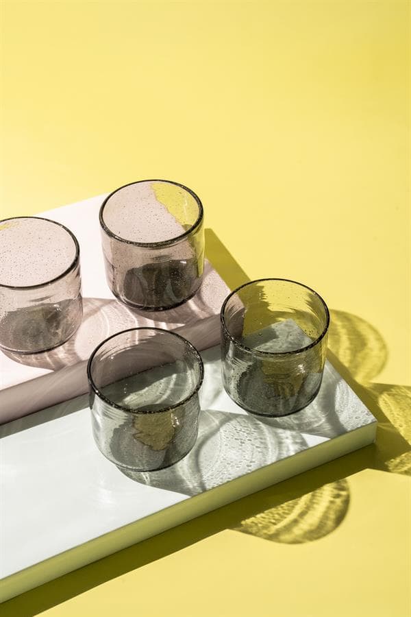 Set van vier glazen op een witte dienblad met een gele achtergrond, stijlvolle en moderne uitstraling, perfect voor interieurdecoratie en servies van Mokana Meubelen.