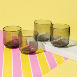 Kleurengetinte glazen bekers op een kleurrijk tafelblad met geel en roze strepen, perfect voor modern interieur en horeca.