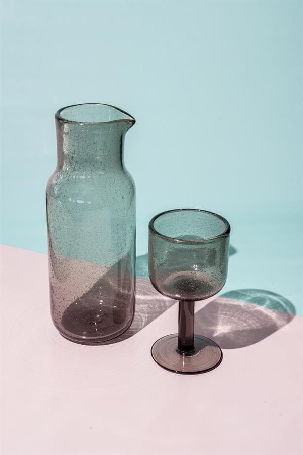 Enkel glasvazen en wijnglas in grijs getint glas, gestyled op een pastelroze en lichtblauwe achtergrond, perfect voor modern interieur en decoratie.