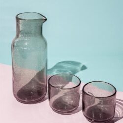 Geglazenisterd vaas en twee bijpassende glazen op een pastelkleurtje achtergrond, modern en stijlvol decoratief glaswerk voor thuis of in een horecaomgeving.