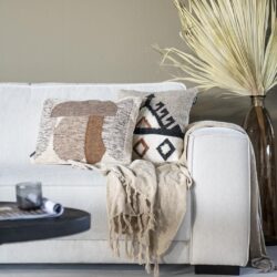 Handgemaakte kussen met geometrisch patroon op een wit banken in een modern woonkamer met natuurlijke decoratie.