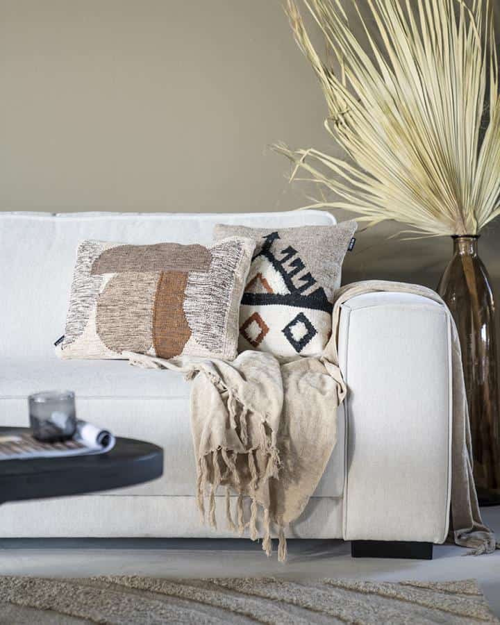 Handgemaakte kussen met geometrisch patroon op een wit banken in een modern woonkamer met natuurlijke decoratie.