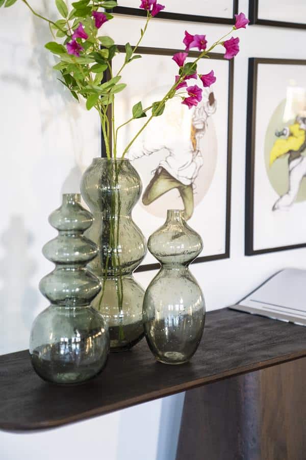 Glazen vazen met decoratieve bloemen op een houten console, geschikt voor modern en industrieel woonkamerinterieur.