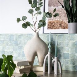 Rustieke vaas met groene eucalyptus takken en decoratieve kaarsen op een wit dressoir, wand met groene tegels, moderne planten en kunstwerk voor een natuurlijke en stijlvolle interieur look.