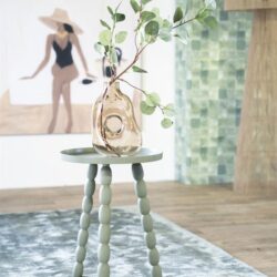 Uniek decoratief bijzettafeltje met gebogen pootjes en een glazen vaas met groene eucalyptus takken, ideaal voor stijlvolle interieurs.