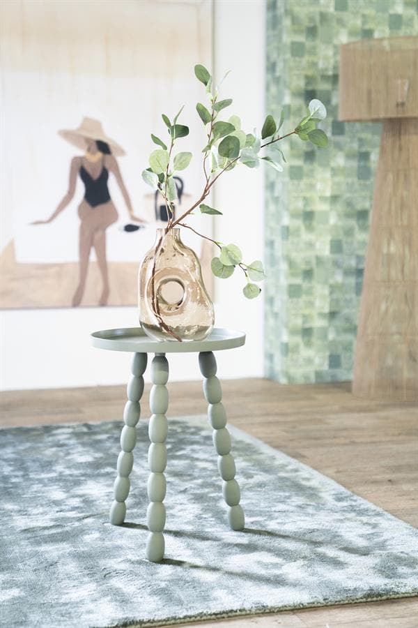 Uniek decoratief bijzettafeltje met gebogen pootjes en een glazen vaas met groene eucalyptus takken, ideaal voor stijlvolle interieurs.