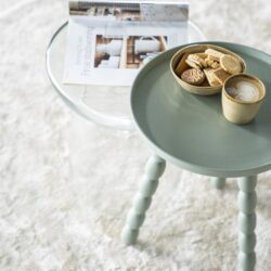 Kleine pastelgroene bijzettafel met poten in de stijl van Mokana meubels, met een schaal vol koekjes en een cappuccino, ideaal voor gezellige momenten en stijlvolle interieuraccenten.