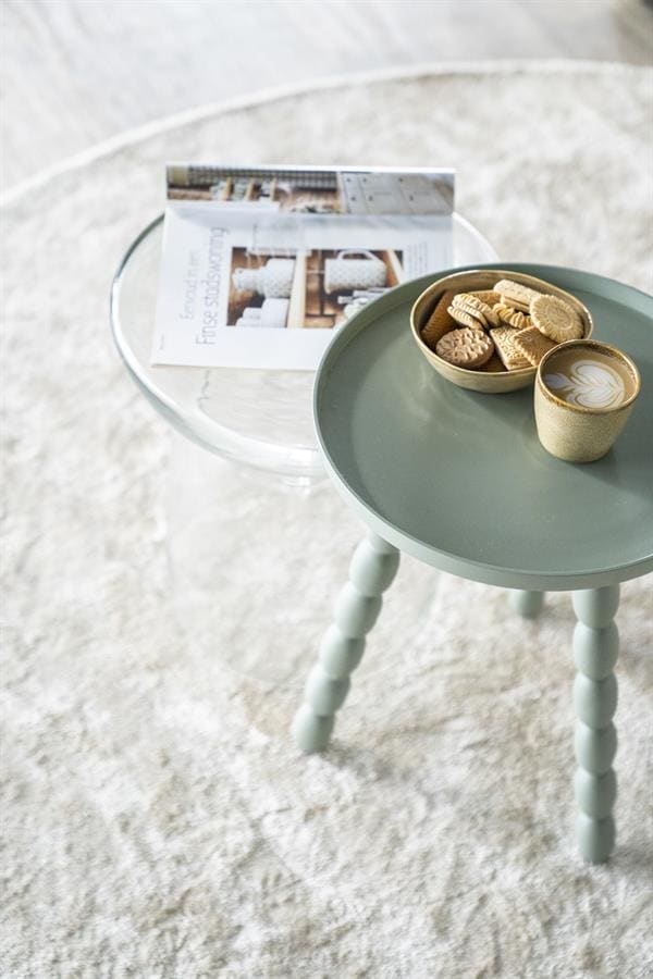 Kleine pastelgroene bijzettafel met poten in de stijl van Mokana meubels, met een schaal vol koekjes en een cappuccino, ideaal voor gezellige momenten en stijlvolle interieuraccenten.
