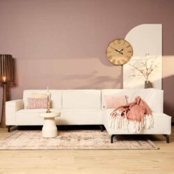 Minimalistische witte hoekbank met witte en roze sierkussens en zachte deken, in een modern woonkamer met pastelmuur en stijlvolle accessoires.