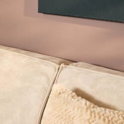 Zachte beige stoffen bank met quilted kussen en roze muur op de achtergrond, moderne woonkamerinrichting, elegant en comfortabel meubilair.