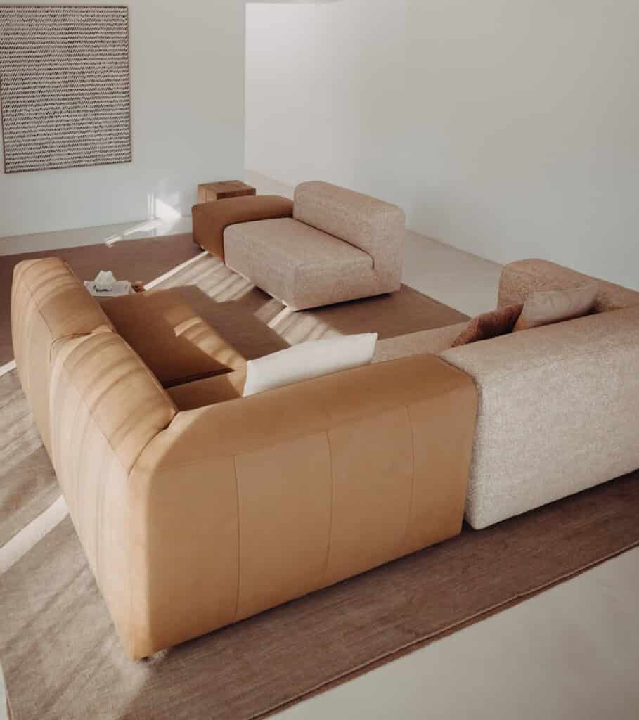 Moderne woonkamer met op maat gemaakte Mokana meubelen, inclusief een luxe cognackleurige bank en beige relaxfauteuils, elegant ingericht met minimalistisch design en natuurlijke kleuren.