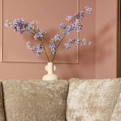 Vaas met zachte pastelblauwe en lavendel bloemen, elegant gedecoreerd in een stijlvolle woonkamer met roze muur en beige bank, perfect voor modern interieurdesign.
