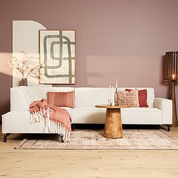 Elegant stoffen bank in een warm, modern interieur met comfortabele sierkussens en een rustieke houten salontafel, perfect voor gezellige woonkamerinrichting.